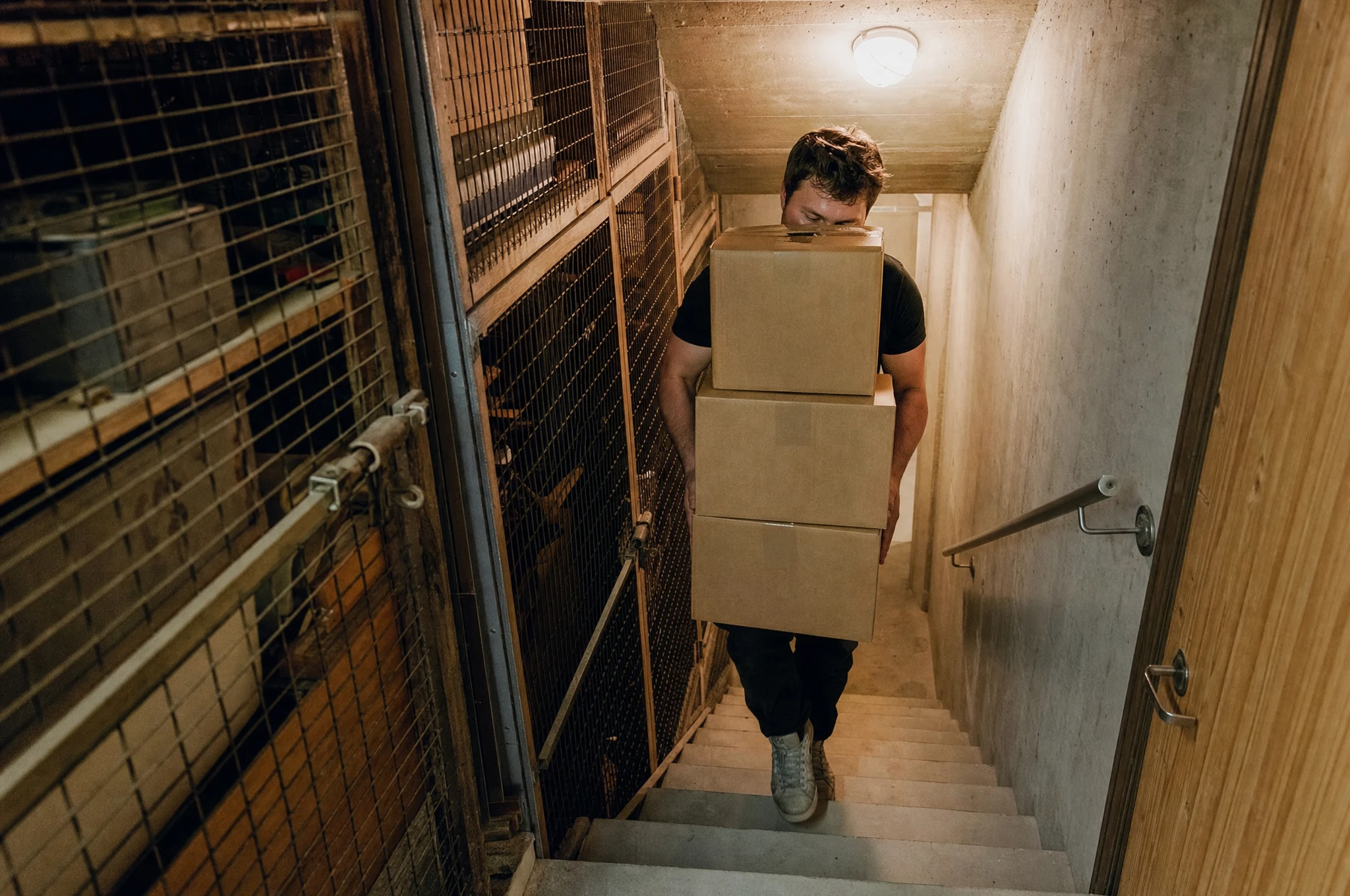 Zuverlässige Kellerräumung und Entsorgung zum Fixpreis – Clearx CLEARX Mitarbeiter trägt schwere Kartons die Kellertreppe hinauf